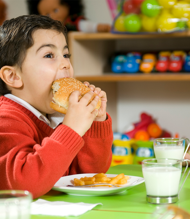 A boy eats a hamburger with a glass of milk.