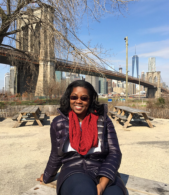 A woman poses for the camera with NYC's Brooklyn Bridge in the background.