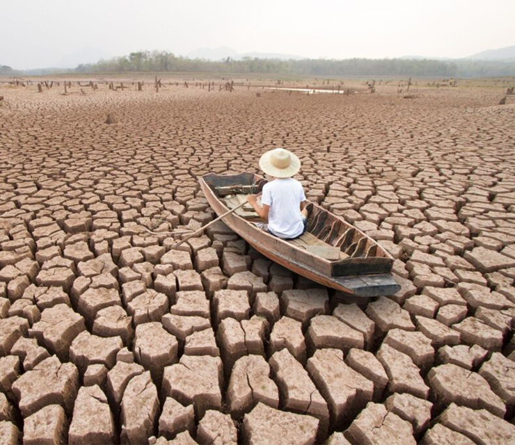 A person sits in a boat in a dried lakebed.